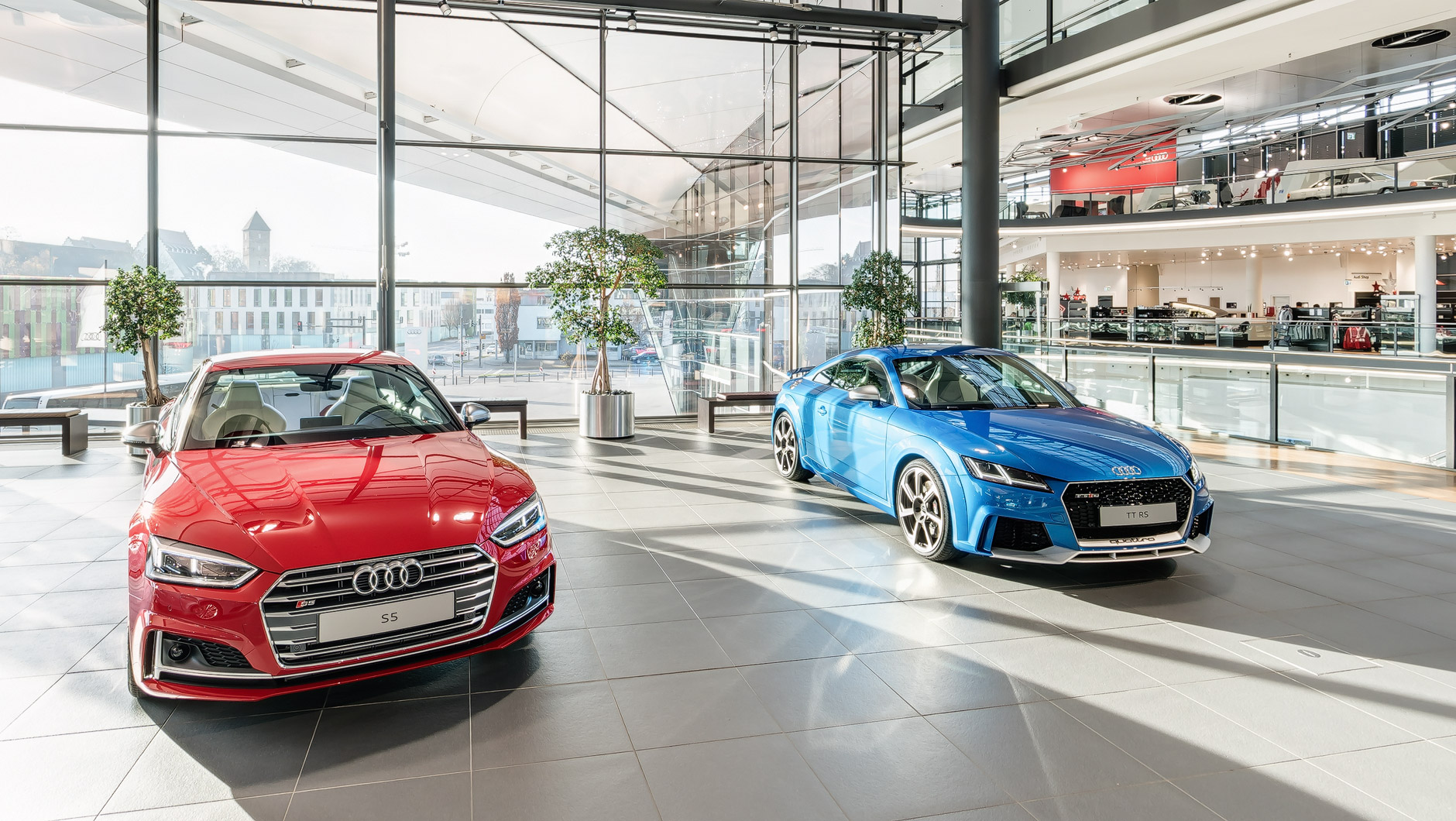 Zwei Audi Modelle im Obergeschoss: ein roter Audi S5 und ein blauer Audi TT RS.