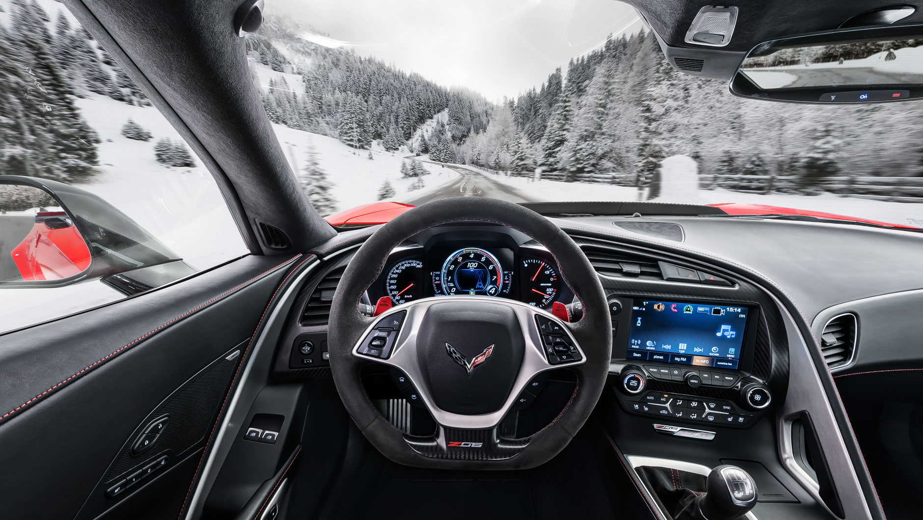 Autoinnenraum / Interieur einer Chevrolet Corvette Z06. Bild aufgenommen aus der Perspektive des Fahrers. Der Sportwagen fährt auf einer Straße in den Alpen umgeben von einer reizvollen Schneelandschaft.